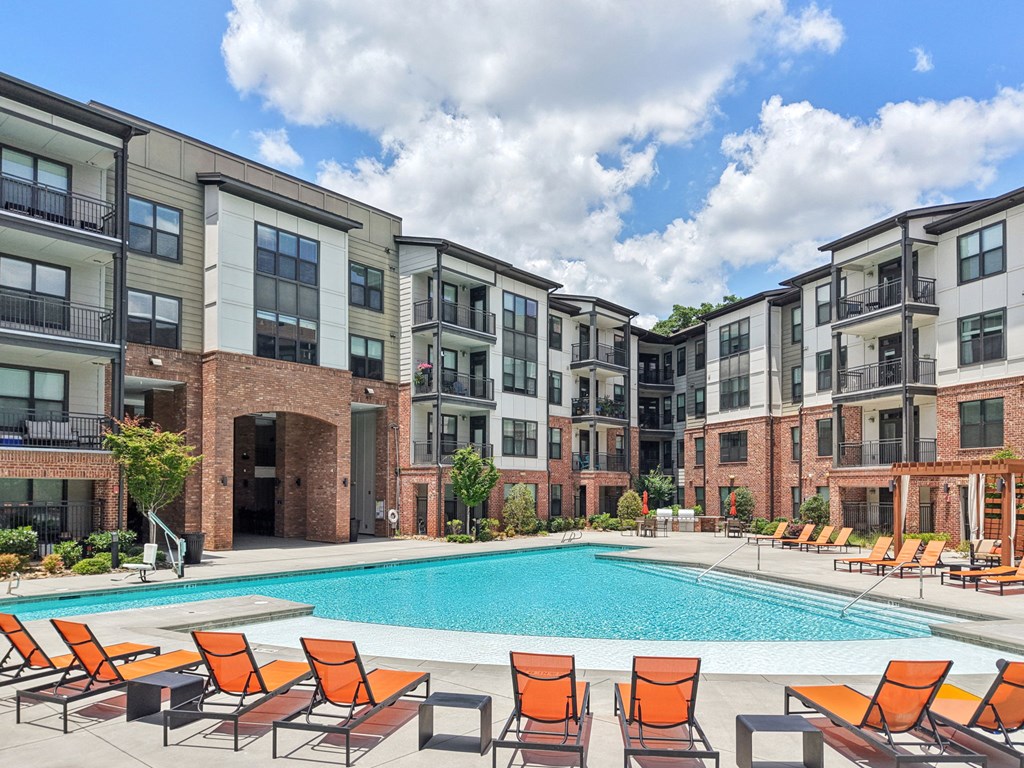 A swimming pool surrounded by orange chairs in front of apartment buildings.